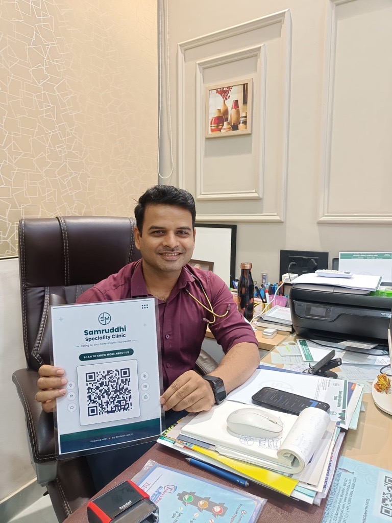 Samruddhi Speciality Clinic doctor holding a ReviewLoop QR flyer at the clinic desk